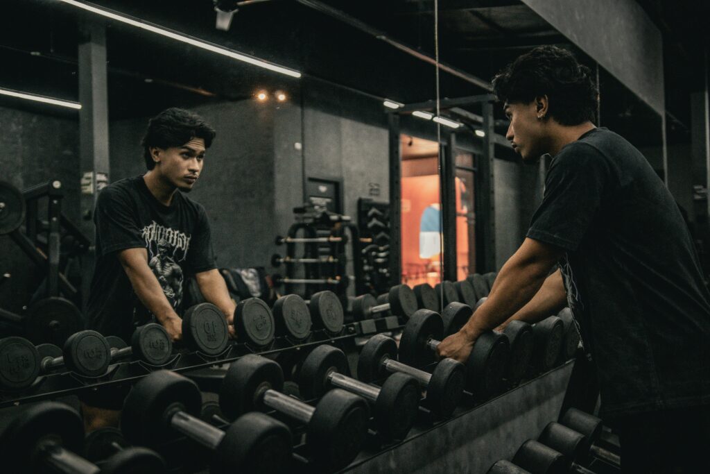 Young man in a gym standing by dumbbells, preparing for strength training and workout session.