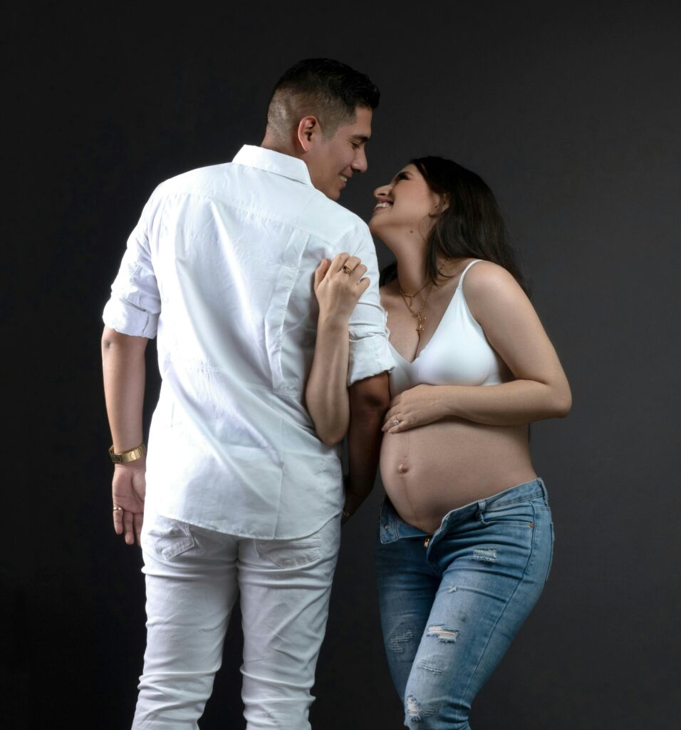 Happy pregnant couple posing together during maternity photoshoot, expecting mother showing baby bump in casual outfit