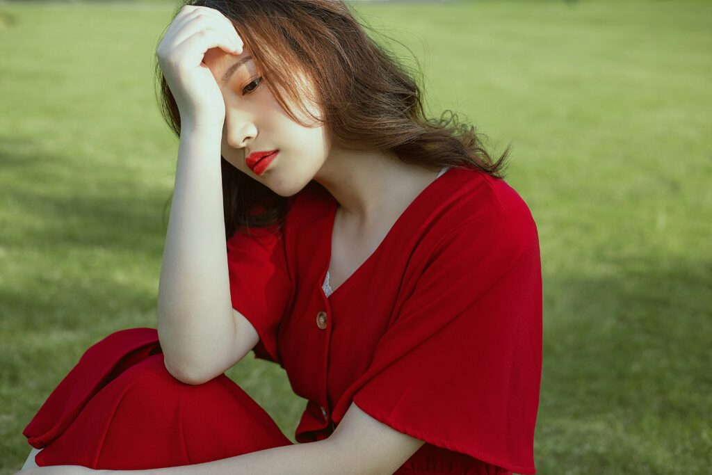 Young woman in a red dress sitting outdoors with a thoughtful and pensive expression on her face.
