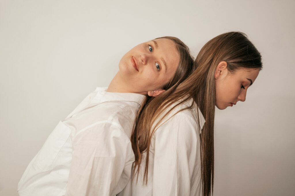 Two young women sitting back to back in white shirts, symbolizing contrast in emotions and relationships