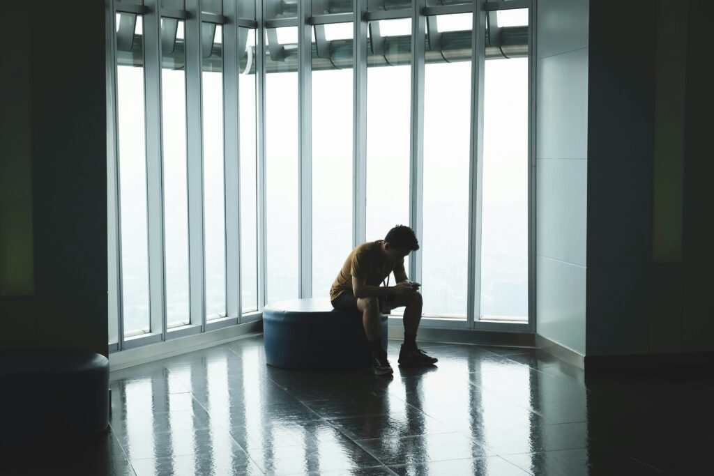 Man sitting alone by large windows reflecting feelings of loneliness and mental health struggles
