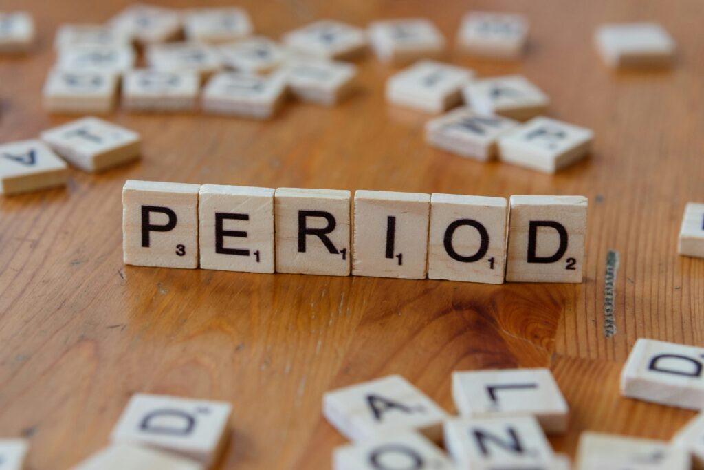 Scrabble letter tiles spelling period on wooden table, symbolizing menstrual cycle and women’s health