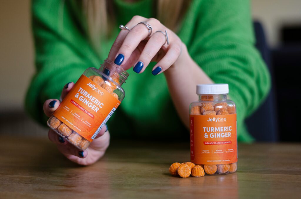 Person holding a bottle of Jellybee Turmeric and Ginger orange flavor gummies, a dietary supplement that supports joint health, reduces inflammation, and aids digestion