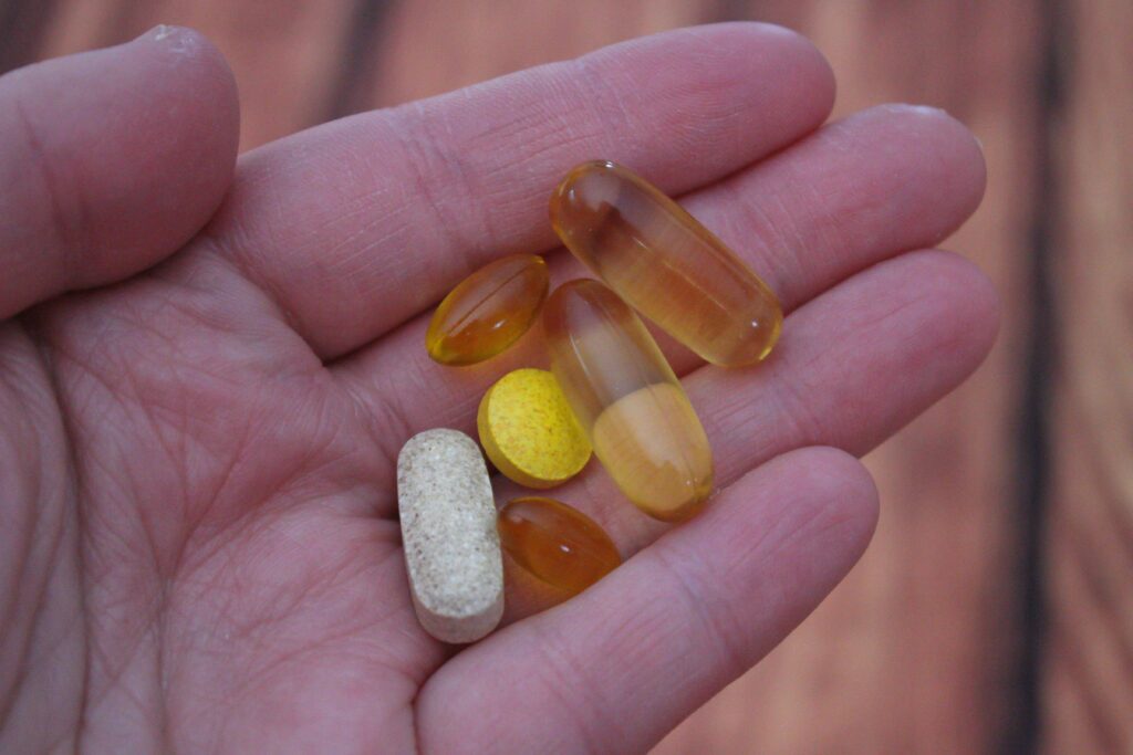 Hand holding different vitamin supplements including multivitamin tablet, omega-3 fish oil capsules, and nutritional pills for daily health support