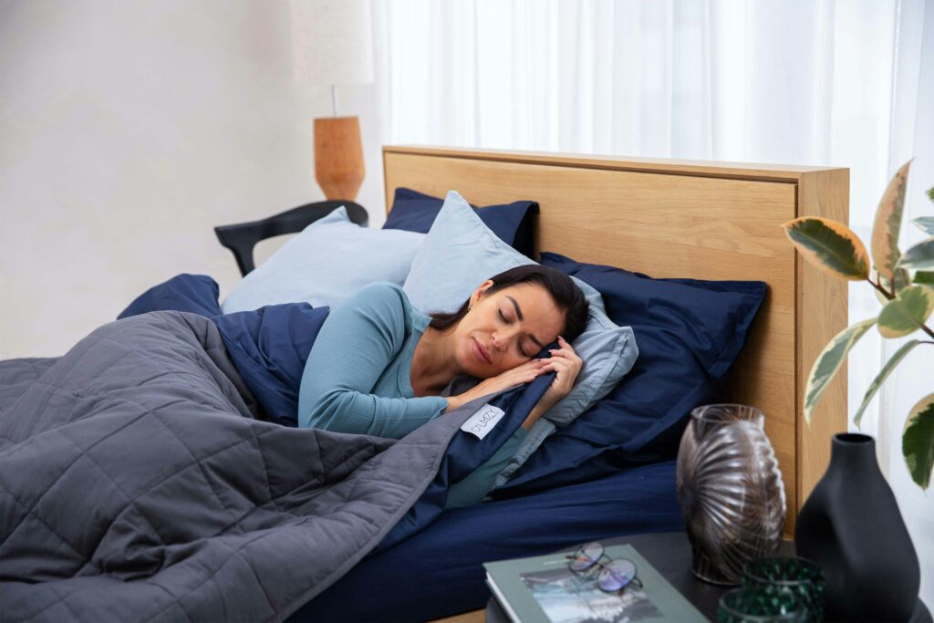 Woman sleeping peacefully on a bed with a weighted blanket, promoting relaxation and better sleep quality
