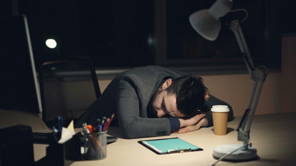 Tired businessman sleeping at his office desk during late-night work, showing exhaustion, work stress, and burnout.