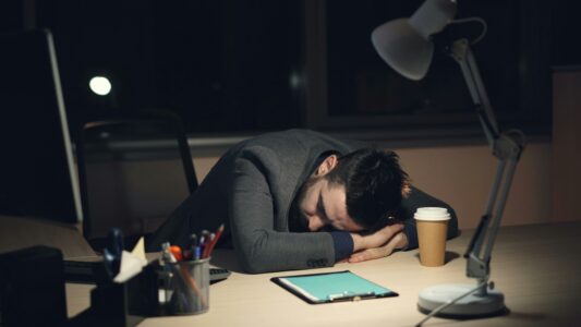 Tired businessman sleeping at his office desk during late-night work, showing exhaustion, work stress, and burnout.