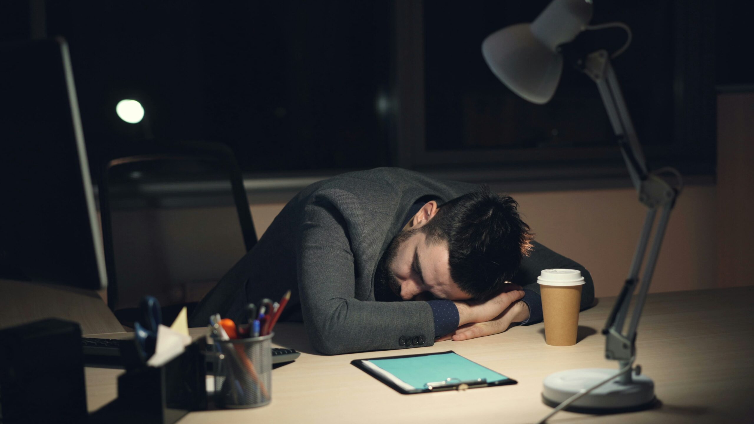 Tired businessman sleeping at his office desk during late-night work, showing exhaustion, work stress, and burnout.