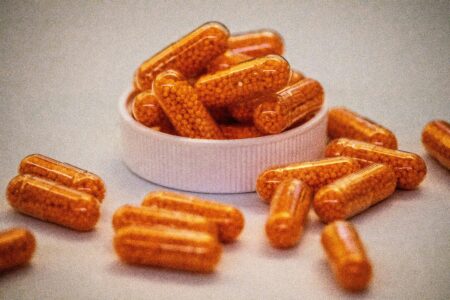 Close-up of turmeric curcumin supplement capsules filled with orange granules in a white container on a light background, representing natural anti-inflammatory and immune support supplements.