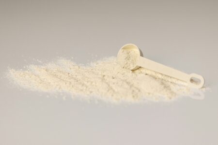 measuring scoop with collagen protein powder supplement spilled on a white surface, nutritional powder for health and fitness