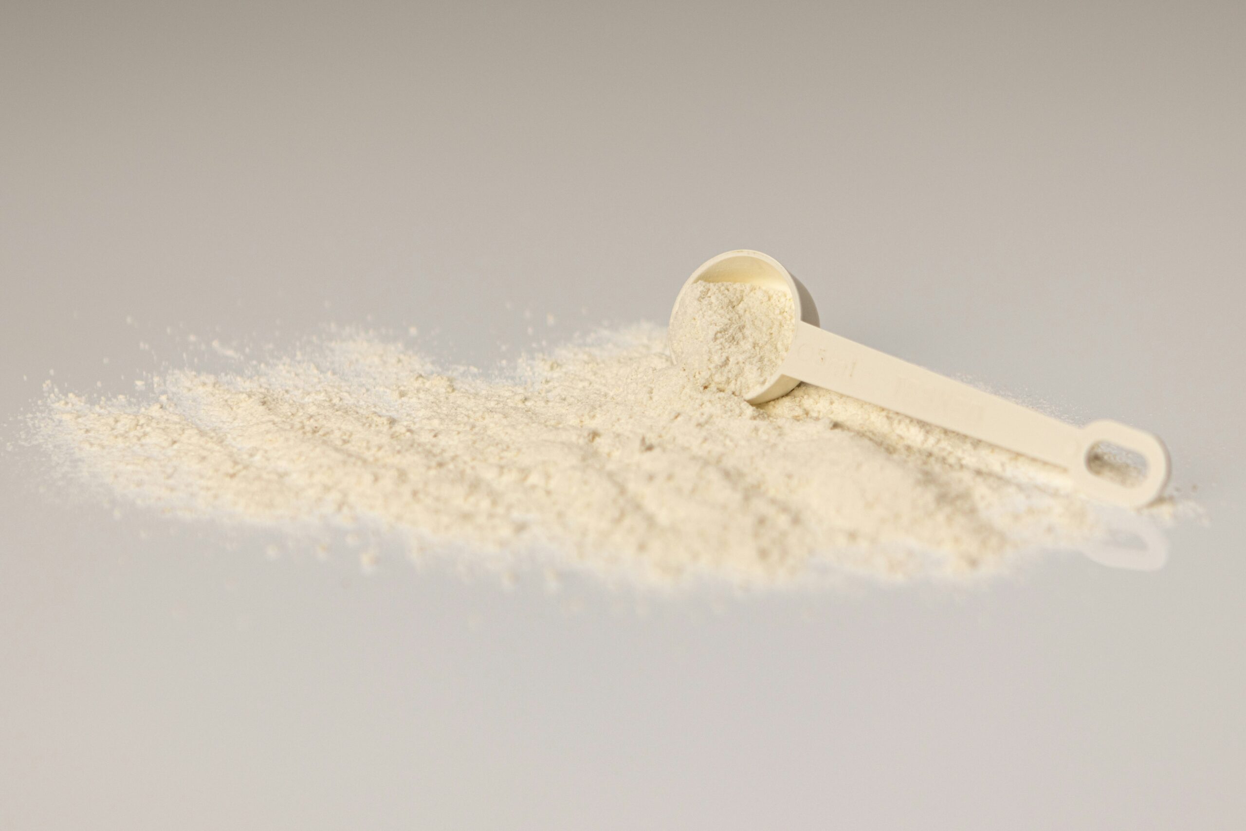 measuring scoop with collagen protein powder supplement spilled on a white surface, nutritional powder for health and fitness